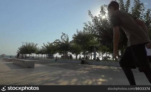 Slow motion steadicam shot of parkour man doing tricks in the city. He is running and sliding on stone benches and making a somersault in bright sunlight