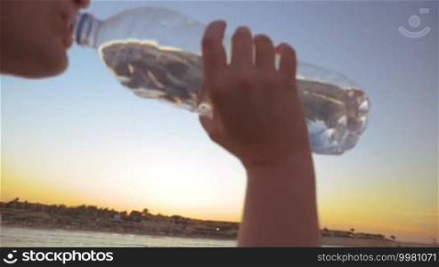 Slow motion steadicam shot of woman drinking water from the bottle and then man joining her after jogging. They refreshing on background of evening sky