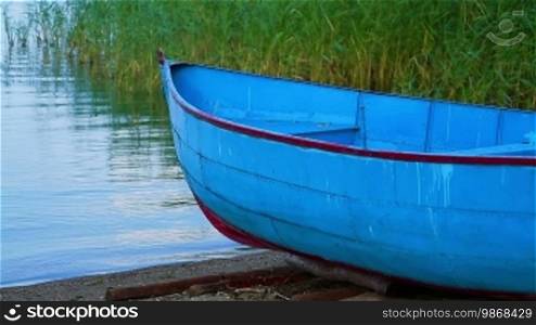 Small blue wooden fishing boat parked on lake beach, close up