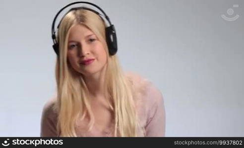 Smiling beautiful girl with earphones enjoying music on white background. Playful cheerful young woman wearing lipstick is listening to music on headphones, flirting to the camera and twisting the headphones wire around her finger.