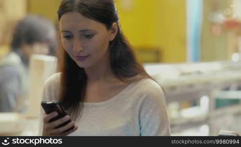 Smiling brunette woman types message using smartphone while sitting in cafe