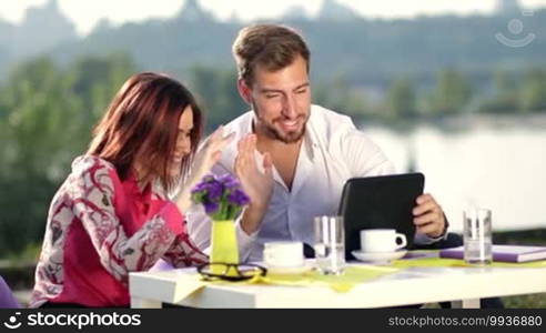 Smiling businesspeople having online meeting using tablet. Two coworkers sitting outdoors during business lunch and having online meeting using digital tablet, person at video conference.