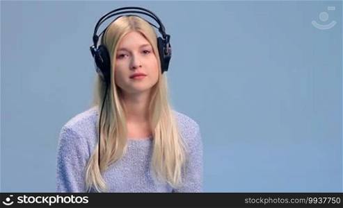 Smiling young woman listening to music in black stylish headphones over white background. Happy teen female with headphones on, touching the earcups with both hands and enjoying music.