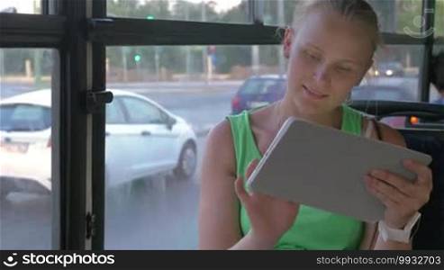 Smiling young woman sitting in bus and using tablet.