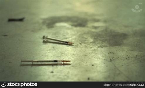 Social issues and substance abuse with syringes used for heroin and drugs on a dirty floor. Low angle, dolly shot