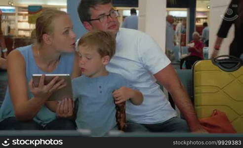 Son is showing to his parents something interesting in tablet PC while they are sitting in airport departure lounge.