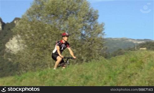 Sports activity and racing: young adult cyclist riding fast mountain bike during race in the countryside