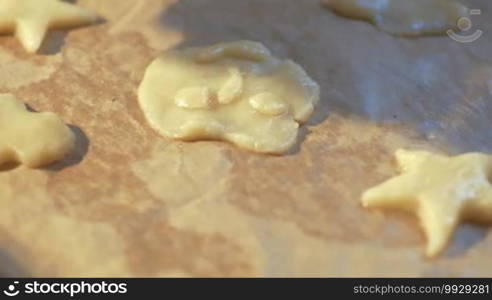 Steadicam and close-up shot of smiley cookie dough on the tray with parchment, then female hands putting star cookies there