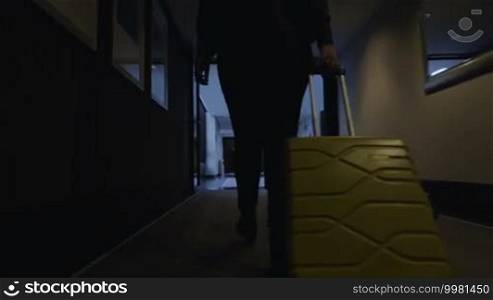 Steadicam and low angle shot of a woman tourist with a roll-on bag walking through the hotel hall and turning to the dimly lit corridor to take a room