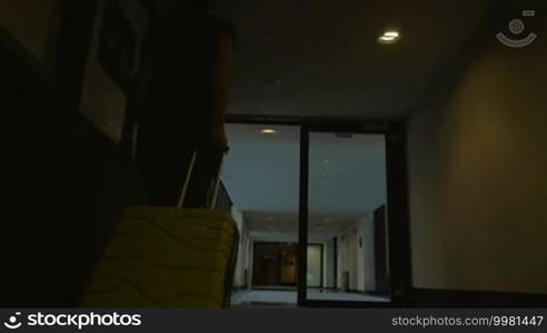 Steadicam and low angle shot of a woman walking along the hotel corridor with yellow trolley bag