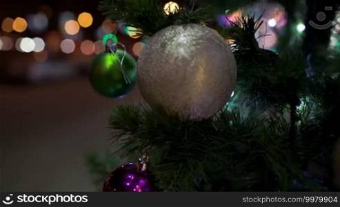 Steadicam close-up shot of an outdoor Christmas tree decorated with colorful balls. Holiday spirit in the night city