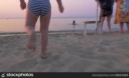 Steadicam shot of a little boy running fast on the sand walking into the sea. He is eager to bathe in warm water in the summer evening