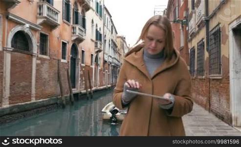 Steadicam shot of a young woman using a tablet PC while walking in Venice. Then following view of a canal and a girl's back view