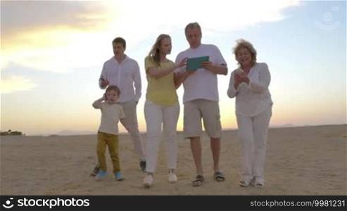 Steadicam shot of big family on vacation with modern gadgets. Everyone is busy with his device. Boy talking on cell phone, father and grandmother using smartphones while mother and grandpa walking with pad. Technology dependence