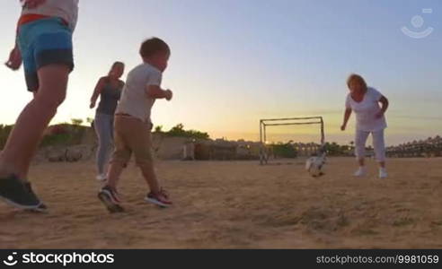 Steadicam shot of family members playing with football on the sand field in the evening.