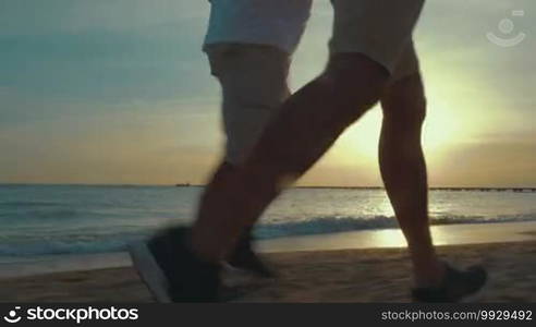 Steadicam shot of father and adult son running alongside the sea early in the morning.