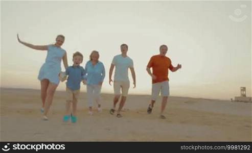 Steadicam shot of happy family on the beach. Parents and grandparents running after little boy and let him to be the first