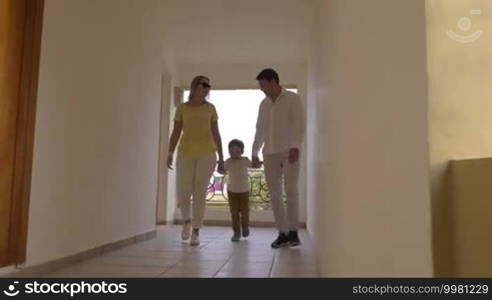Steadicam shot of mother, father, and little son in hotel corridor. Happy naughty boy escaping from parents and running along the hall