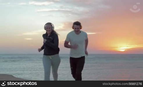 Steadicam shot of two friends jogging on the beach. Setting sun is shining upon their backs.