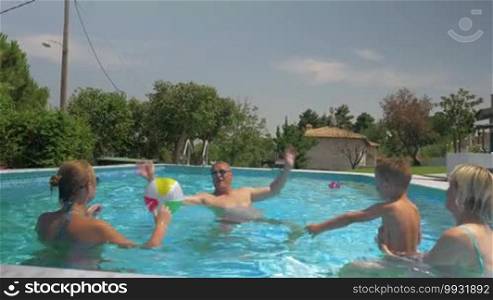 Steadicam shot of united family playing inflatable ball in their open-air home pool on a sunny day.