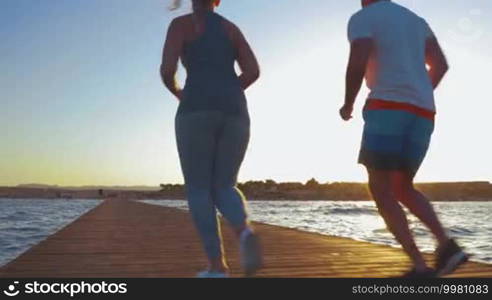 Steadicam shot of young couple ending their morning jogging. They are running turned backs to the camera, then make a jump and deep breath.