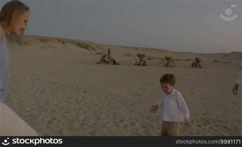 Steadicam shot of young parents and little son playing football on the beach at sunset. Outdoor activity with child