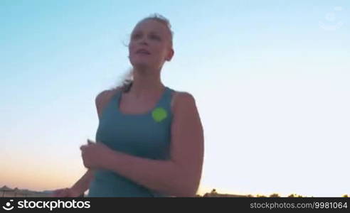 Steadicam shot of young woman having everyday run on background of evening sky. Regular jogging keeps healthy and fit