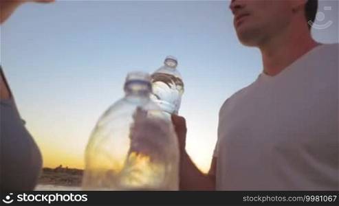 Steadicam slow motion shot of male and female persons drinking water from plastic bottles.