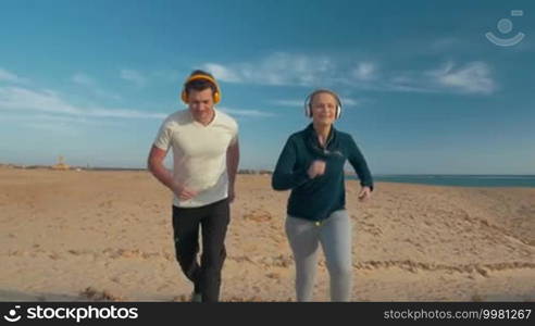 Steadicam slow motion shot of two friends running alongside the sea. They are moving towards the camera.