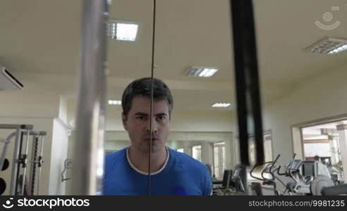 Strong and serious man being fully concentrated on his workout on pull down machine. Moving weight blocks in foreground