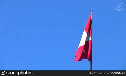 Swiss flag flutters against a blue sky