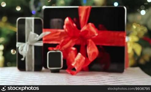Tablet PC, smartphone, and smartwatch as gifts in front of Christmas tree with lights.
