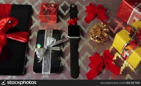 Tablet PC, smartphone, and smartwatch for Christmas with gifts and decorations on the table.