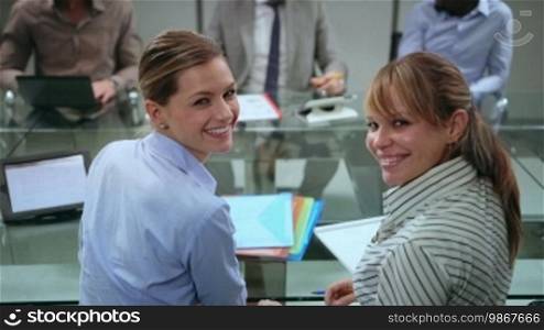 Team of business people working and talking during a meeting in an office room, with a portrait of female coworkers smiling and looking at the camera. 10 of 20