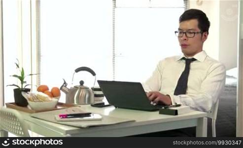 Technology and Asian people working at home with PC, young business man at work with laptop computer while having breakfast in living room, businessman talking on mobile phone, busy male manager