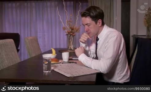 Technology and people working at home, young business man at work with mobile phone and newspaper, businessman having breakfast in living room, busy manager talking on smartphone in the morning