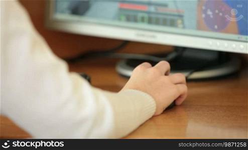 Teen boy playing desktop computer games, focus on the hand with computer mouse, closeup