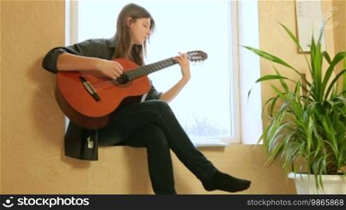 Teen girl learning to play guitar at home. Long shot