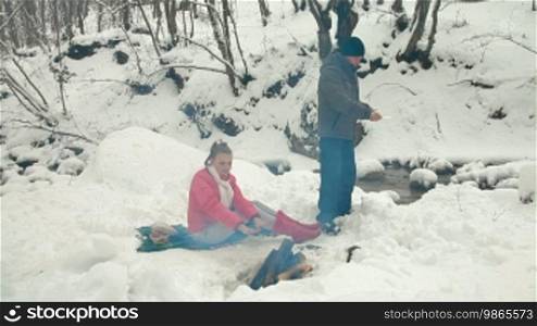Teenage couple enjoying winter holidays near campfire in snowy forest