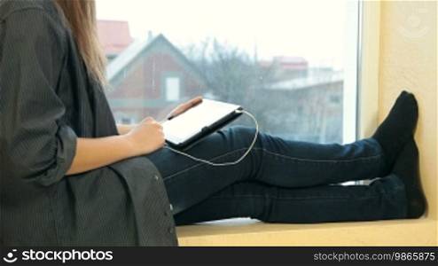 Teenage girl surfing the net and listening to music on a tablet computer at home