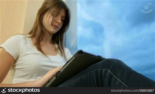 Teenager girl listening to music on a digital tablet, looking through the window