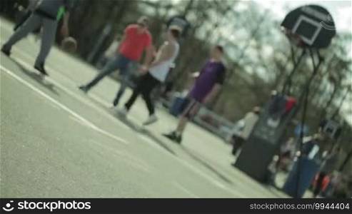Teenagers playing basketball in a city park. Blurred with empty surface in front.