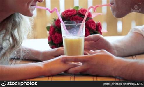 The bride and groom drink orange juice from one glass at a cafe