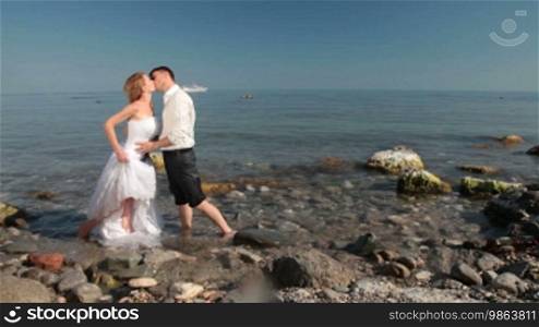 The bride and groom kissing on the beach with a sailing ship in the background
