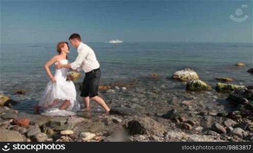 The bride and groom kissing on the beach, with a sailing ship in the background