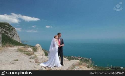 The bride and groom on a cliff against the blue sky and sea