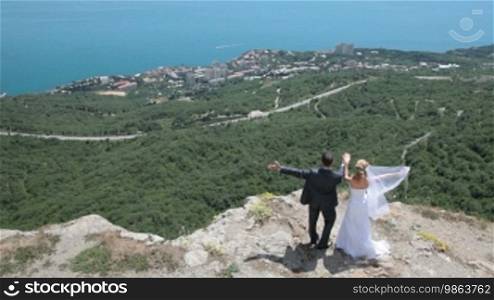 The bride and groom on a cliff against the blue sky and sea