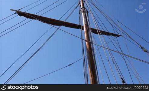 The rigging of a large sailing ship/windjammer sways in the wind against a blue sky