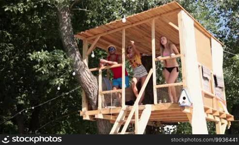 Three friends on vacation looking at sea from tree house. Group of friends enjoying beach holiday talking and relaxing