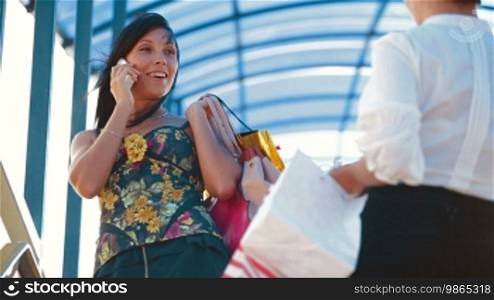 Three smiling women with shopping bags converse with excitement on a city street